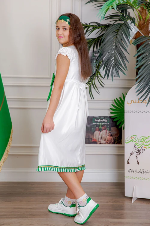 فستان بناتي لون أبيض مزين بتطريز اليوم الوطني ياقة دائرية بأكمام قصيرة و فيونكة من الأمام و رباط من الخلف