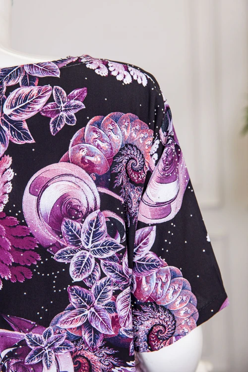 قميص نسائي طويل لون أسود مشجر باللون الموف مزين بفصوص ياقة دائرية بأزرار من الأمام و أكمام قصيرة