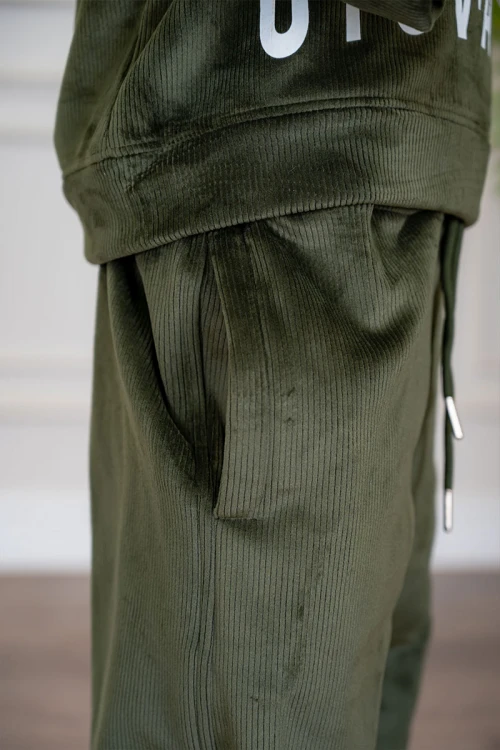 طقم بناتي شتوي قطعتين لون زيتي هودي بقبعة متصلة برباط و أكمام طويلة مزين بكتابات باللون الأبيض مع بنطلون طويل برباط في الخصر و جيوب من الجانبين