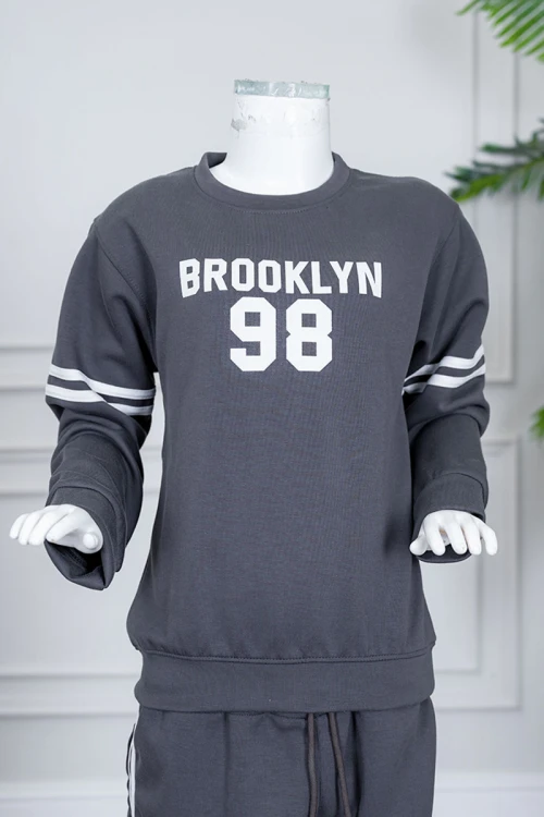 طقم بناتي شتوي قطعتين لون رصاصي بلوزة بياقة دائرية مزين بكتابات و خطوط باللون الأبيض بأكمام طويلة مع بنطلون طويل برباط في الخصر و جيوب من الجانبين