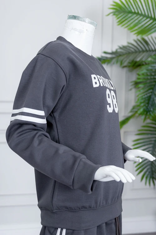 طقم بناتي شتوي قطعتين لون رصاصي بلوزة بياقة دائرية مزين بكتابات و خطوط باللون الأبيض بأكمام طويلة مع بنطلون طويل برباط في الخصر و جيوب من الجانبين