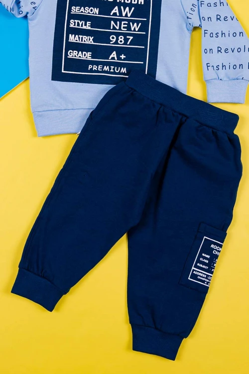 طقم قطعتين ولادي بلوزة لون سماوي مزينة بكتابات من الأمام و الخلف و بأكمام طويلة مع بنطلون كحلي طويل برباط في الخصر و زم في الأطراف