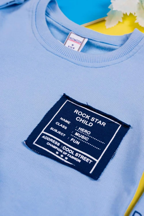 طقم قطعتين ولادي بلوزة لون سماوي مزينة بكتابات من الأمام و الخلف و بأكمام طويلة مع بنطلون كحلي طويل برباط في الخصر و زم في الأطراف