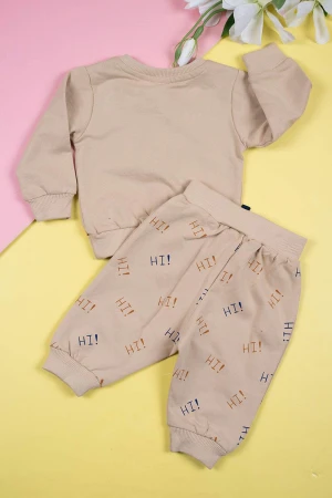طقم قطعتين ولادي لون بيج بلوزة مزينة بكتابات ورسومات و أزرار من الأمام و بأكمام طويلة مع بنطلون طويل برباط في الخصر و زم في الأطراف