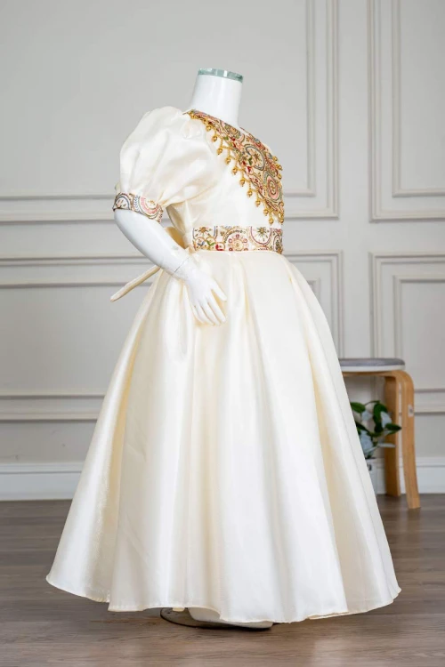 فستان بناتي طويل لون بيج فاتح مزين بتطريز ملون من الياقة و أطراف الأكمام و بحزام في الخصر