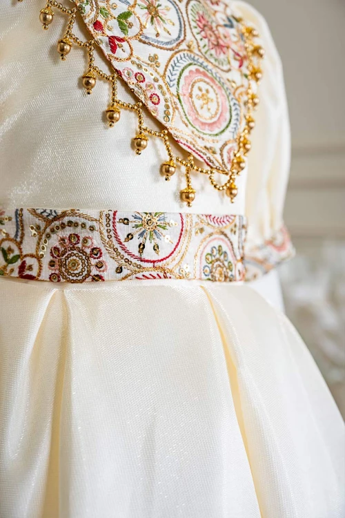 فستان بناتي طويل لون بيج فاتح مزين بتطريز ملون من الياقة و أطراف الأكمام و بحزام في الخصر