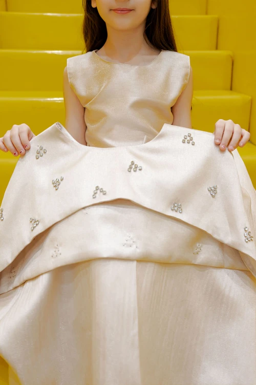 فستان بناتي لون بيج ياقة دائرية بدون أكمام مع فيونكة من الأمام و رباط في الخصر و بكاب علوي منفصل على الكتف مزين بفصوص الكريستال