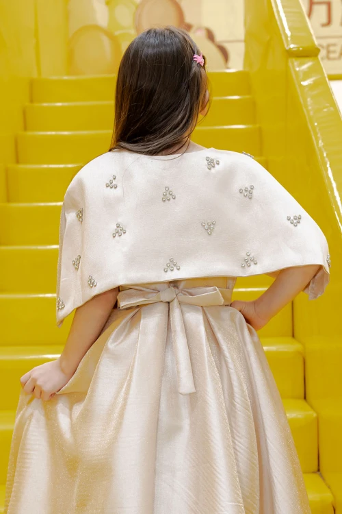 فستان بناتي لون بيج ياقة دائرية بدون أكمام مع فيونكة من الأمام و رباط في الخصر و بكاب علوي منفصل على الكتف مزين بفصوص الكريستال
