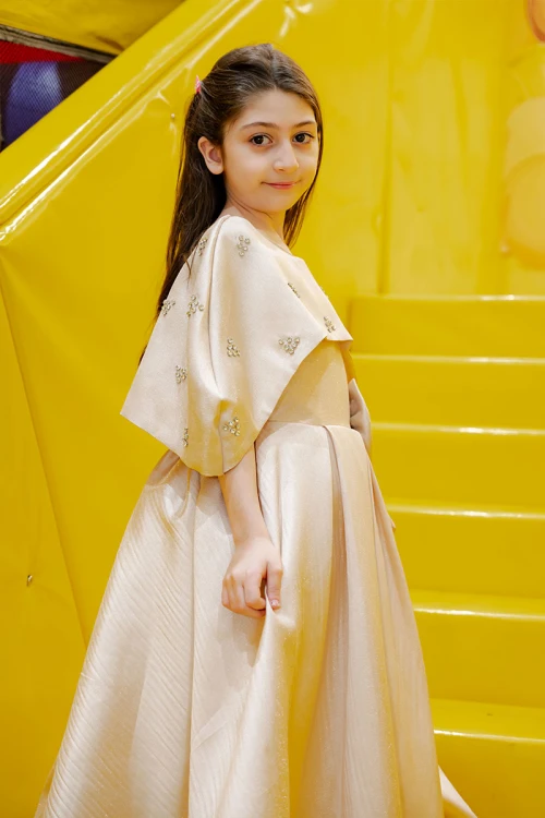 فستان بناتي لون بيج ياقة دائرية بدون أكمام مع فيونكة من الأمام و رباط في الخصر و بكاب علوي منفصل على الكتف مزين بفصوص الكريستال