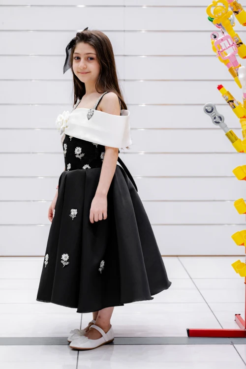 فستان بناتي لون أسود و أبيض بأكتاف مكشوفة و فيونكة بيضاء من الأمام مزين بتطريز على شكل ورود و برباط في الخصر