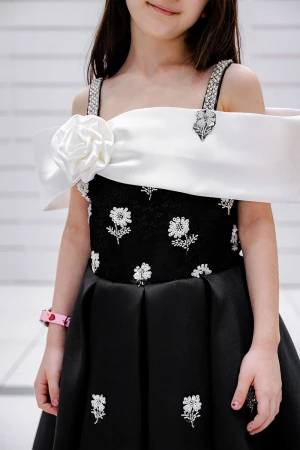 فستان بناتي لون أسود و أبيض بأكتاف مكشوفة و فيونكة بيضاء من الأمام مزين بتطريز على شكل ورود و برباط في الخصر 