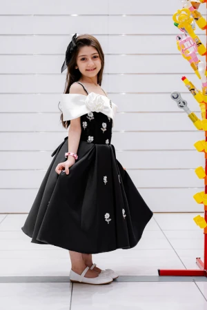 فستان بناتي لون أسود و أبيض بأكتاف مكشوفة و فيونكة بيضاء من الأمام مزين بتطريز على شكل ورود و برباط في الخصر 