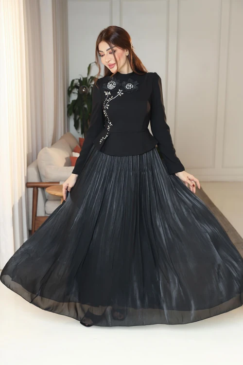 فستان نسائي لون أسود ياقة عالية بأكمام طويلة مزين بتطريزات على شكل زهور بكريستالات من الأمام مع تنورة كسرات