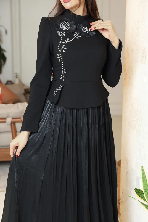 فستان نسائي لون أسود ياقة عالية بأكمام طويلة مزين بتطريزات على شكل زهور بكريستالات من الأمام مع تنورة كسرات