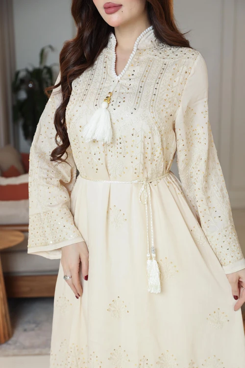 جلابية نسائية لون بيج ياقة عالية بقصة سبعة مزينة بالترتر و تطريزات ذهبية و بأكمام طويلة مع رباط في الخصر