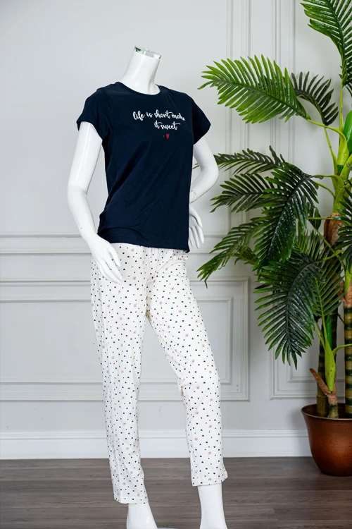 بيجاما نسائية قطعتين بلوزة لون كحلي بياقة دائرية مزينة بكتابات من الأمام و بأكمام قصيرة مع بنطلون اوف وايت طويل مزين بالقلوب