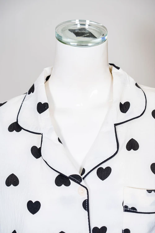 بيجاما نسائية قطعتين لون اوف وايت مزينة بقلوب باللون الأسود  بلوزة بياقة مطوية بجيب من الأمام و أكمام قصيرة مع بنطلون طويل