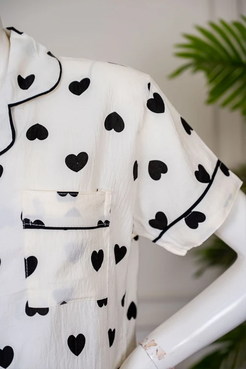 بيجاما نسائية قطعتين لون اوف وايت مزينة بقلوب باللون الأسود  بلوزة بياقة مطوية بجيب من الأمام و أكمام قصيرة مع بنطلون طويل