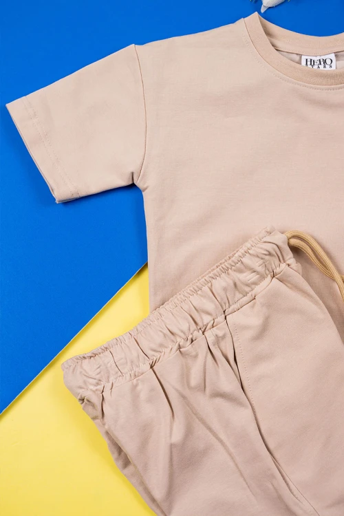 طقم ولادي قطعتين لون بيج تيشيرت بكتابات و رسومات من الأمام مع شورت برباط في الوسط و جيوب من الجانبين