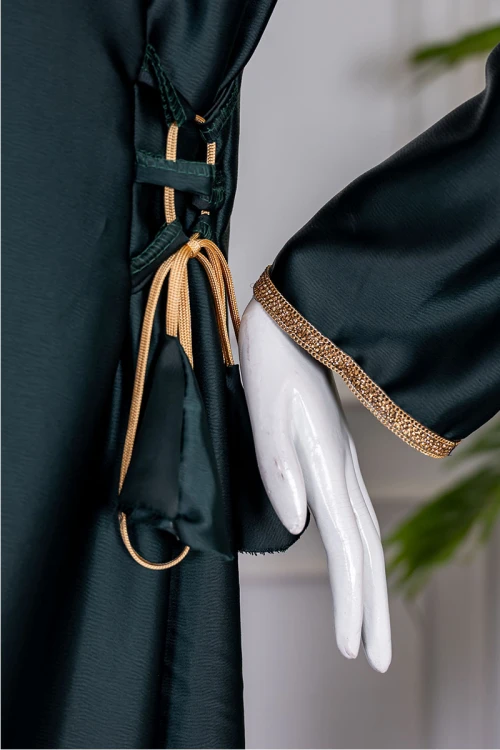 جلابية نسائية لون زيتي ياقة بقصة سبعة مزينة بكلفة مطرزة باللون الذهبي من الياقة و أطراف الأكمام و برباط من الجانبين