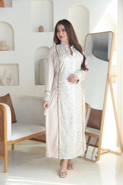 جلابية نسائية طويلة لون اوف وايت مزينة بتطريزات هندسية باللون الفضي و الذهبي من الأمام و الأكمام ياقة عالية بقصة سبعة و برباط في الجانبين لتحديد الخصر