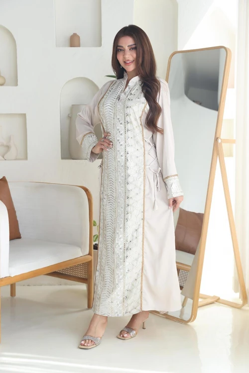 جلابية نسائية طويلة لون اوف وايت مزينة بتطريزات هندسية باللون الفضي و الذهبي من الأمام و الأكمام ياقة عالية بقصة سبعة و برباط في الجانبين لتحديد الخصر